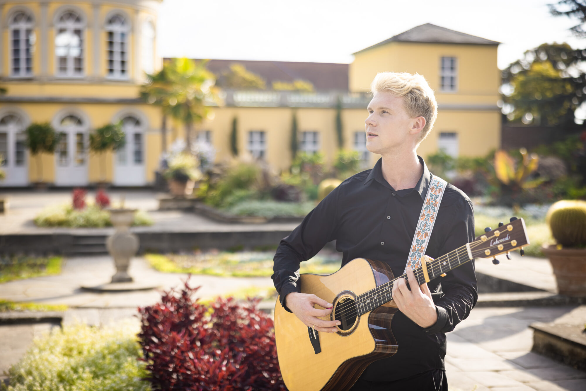 Leon singt mit Gitarre bei Sonnenschein im Berggarten Hannover.